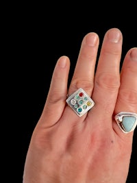 a person's hand holding a ring with turquoise stones