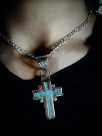 a person wearing a necklace with a turquoise cross on it