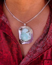 a woman wearing a necklace with a turquoise stone