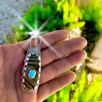a hand holding a silver pendant with a turquoise stone