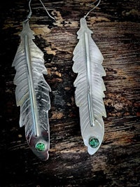 a pair of silver feather earrings with emerald stones