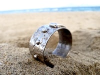 a silver ring sitting in the sand next to the ocean